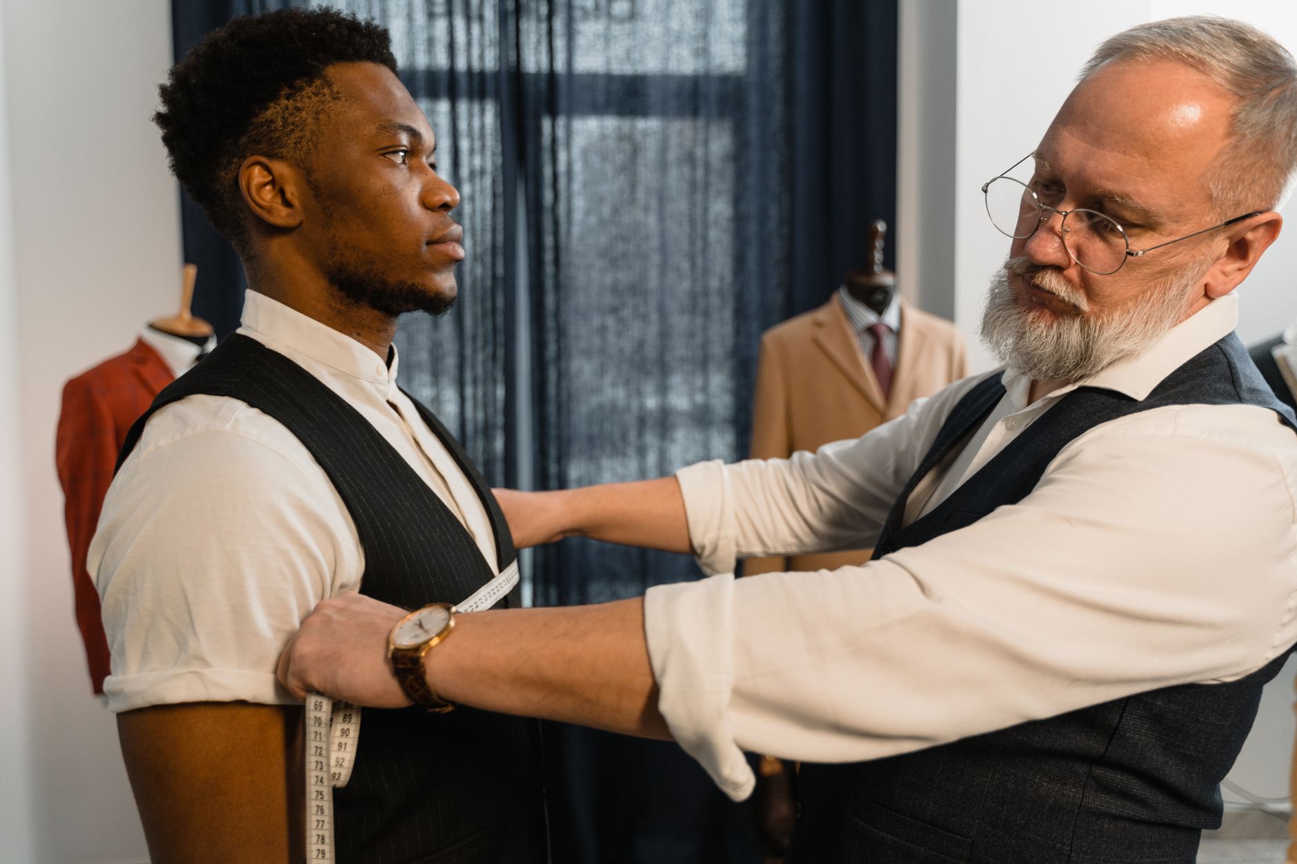 Professional tailor takes measurements for a bespoke suit fitting in a tailoring workshop.